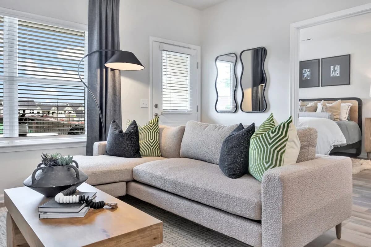 Maymont Homes living room with navy and green accent pillows, coffee table, and floor lamp with natural lighting